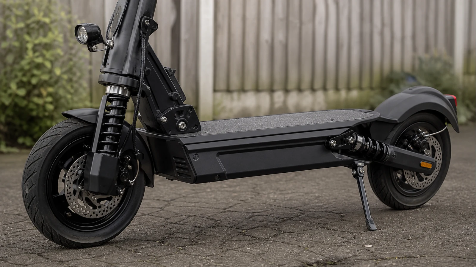 Adult electric scooter dual suspension components above uneven private tarmac